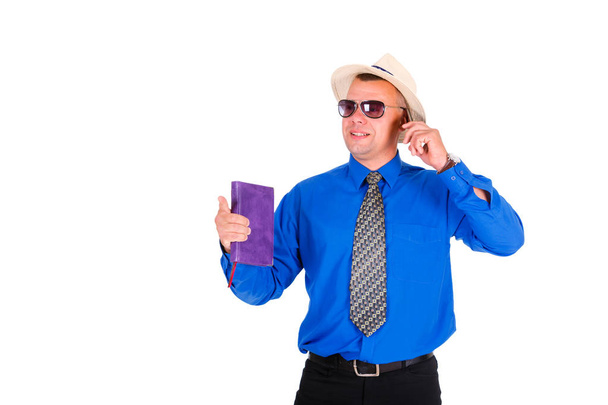 Ευτυχισμένος και χαμογελαστός επιχειρηματίας με μπλε πουκάμισο, γραβάτα, γυαλιά ηλίου και λευκό καπέλο. Μιλώντας από κινητό τηλέφωνο και κρατώντας το σημειωματάριο στο χέρι. Απομονωμένο λευκό φόντο, έννοια της ηγεσίας και της επιτυχίας - Φωτογραφία, εικόνα