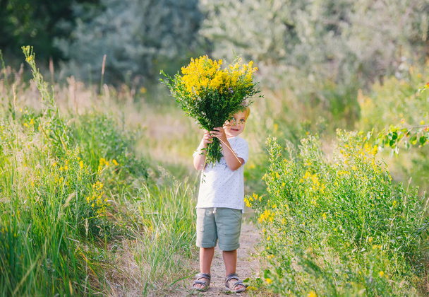 Happy child boy with bouquet of wild flowers in his hands enjoying for mother. - Фото, изображение