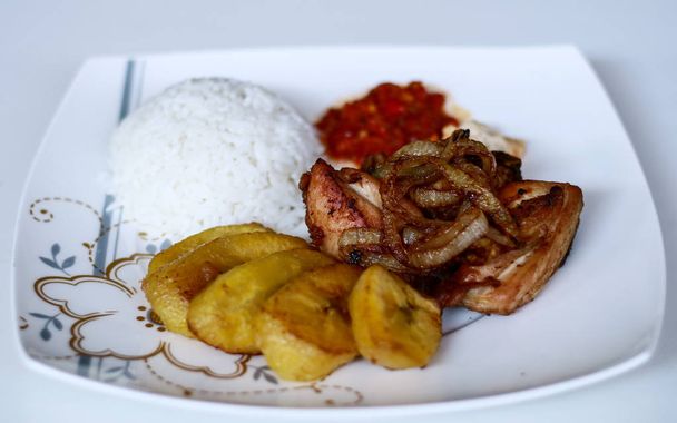 Pollo fritto africano con banane fritte, riso, cipolle fritte, salsa di peperoncino e salsa di candele
. - Foto, immagini