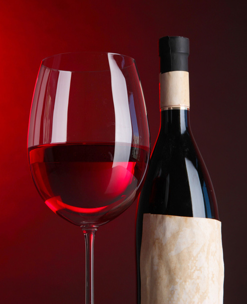 Glass of wine with bottle on bright red background - Foto, imagen
