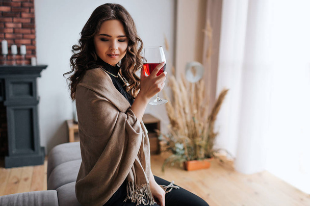 Young businesswoman work at home. Hold glass of red wine in hand. Beautiful model in evening dress stand at window. Alone in room. - Foto, Imagen