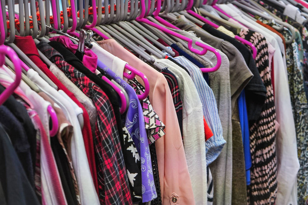 verschiedene Frauenkleider auf meist rosafarbenen Kleiderbügeln in einem wohltätigen Second-Hand-Laden - Foto, Bild