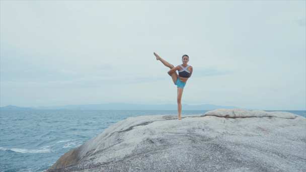 Mujer de pie sobre una pierna y meditando sobre rocas cerca del océano
 - Imágenes, Vídeo