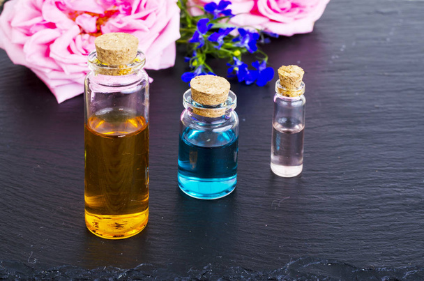 Три бутылки эфирного масла со свежими цветами на черном фоне
 - Фото, изображение