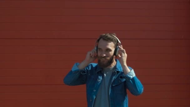Happy young man with headphones. Listening to music and dancing on a red background. slow motion - Video