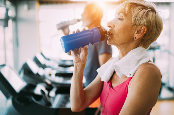 Senior woman drinking water in gym after workout - Photo, image