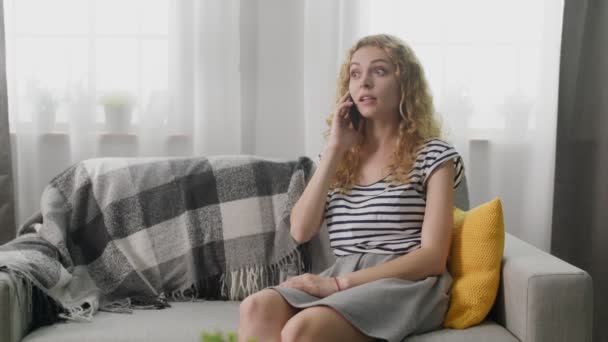 Girl talking on a mobile phone at home on the sofa - Materiał filmowy, wideo