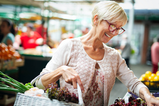 Picture of senior happy woman at marketplace buying vegetables - Fotó, kép