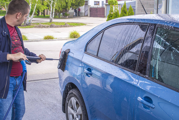 Using a brush to wash a car on a car washing facility on sunny summer day.Manual car wash with pressurized water in car wash outside.Blue car manual wash of with pressurized water in car wash outside. - Photo, Image