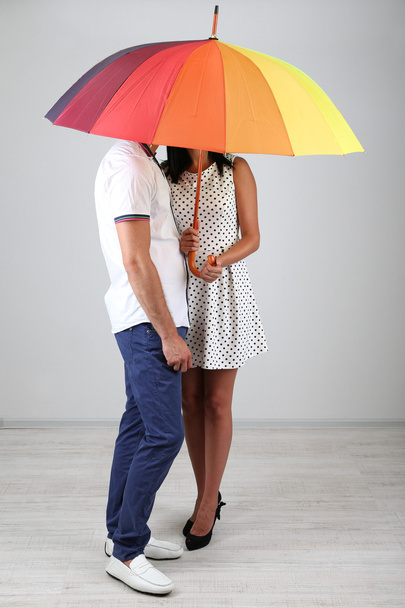 Beautiful loving couple with umbrella on grey background - Photo, image