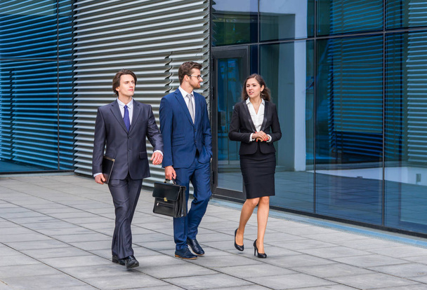 Confident businesspersons talking in front of modern office building. Businessmen and businesswoman have business conversation. Banking, professional job and financial market concept. - Foto, imagen