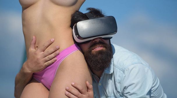 The world of erotic virtual reality. Bearded man in virtual reality headset hugging sexi topless woman. Hipster wearing virtual reality device touching sexy girl body. Adult virtual reality games - 写真・画像