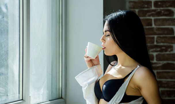 Best thing to drink in the morning. Adorable girl holding cup with tasty coffee drink. Sexy woman enjoying her drink recipe. Pretty woman drinking healthy morning drink at window - 写真・画像