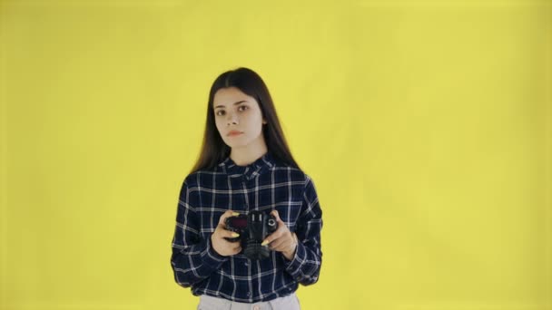Νεαρό κορίτσι κοιτάζοντας κάμερα και τη λήψη φωτογραφιών σε κίτρινο φόντο στο στούντιο - Πλάνα, βίντεο