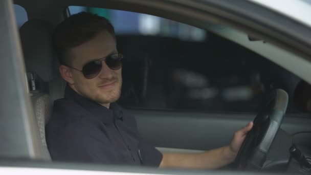 Cheerful male cop wearing sunglasses sitting in patrol car and smiling at camera - Footage, Video