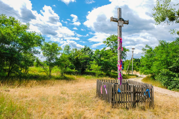 Старый деревянный крест с розовыми лентами на перекрестке песчаных дорожек на окраине исчезающего села Сваловичи в Украине. Украинская ПОЛИСЯ
. - Фото, изображение