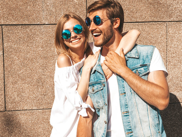 Smiling beautiful girl and her handsome boyfriend. Woman in casual summer dress.Man in jeans clothes.Happy cheerful family.Female having fun on the street near wall.Hugging couple in sunglasses - Fotoğraf, Görsel
