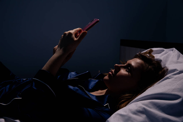 Дівчина лежить в ліжку і використовує мобільний телефон вночі
. - Фото, зображення