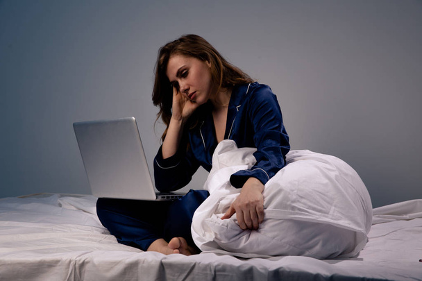 Kuva väsynyt ja tylsistynyt nainen kotona istuu tietokoneen kanssa sängyssä yöllä
. - Valokuva, kuva