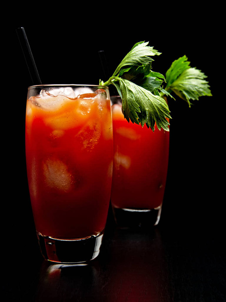 Bloody Mary drinks with ice cubes and celery isolated on black - Фото, изображение