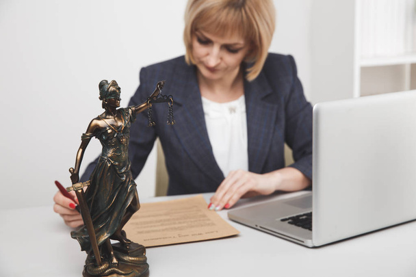 オフィスの女性弁護士が座って紙とノートパソコンを操作. - 写真・画像