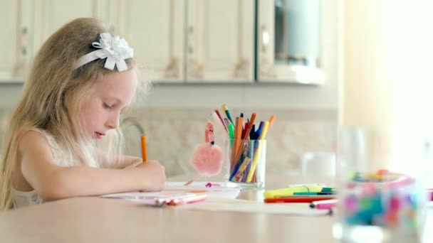 Een schattig klein meisje zit aan haar Bureau en tekent met potloden - Video