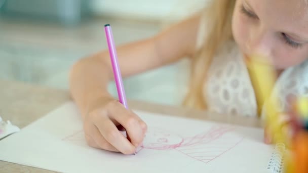 Söpö pikkutyttö istuu pöydässä ja piirtää kynillä
. - Materiaali, video