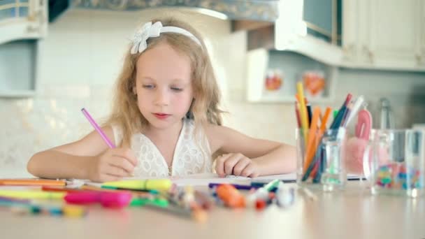 Söpö pieni tyttö istuu pöytänsä ääressä ja piirtää kynillä
 - Materiaali, video