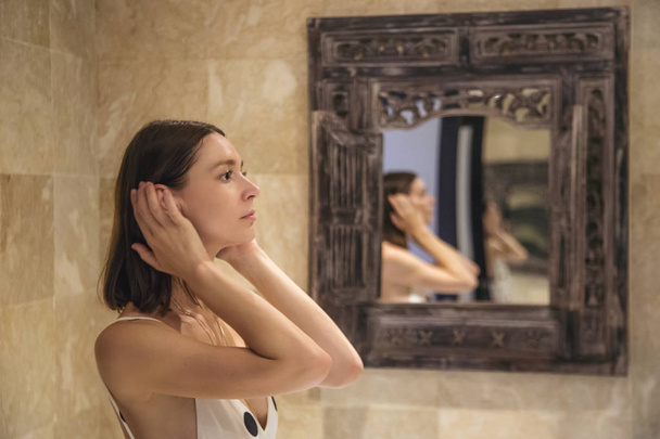 Portrait of a young woman standing in the bathroom in front of the mirror - Foto, immagini