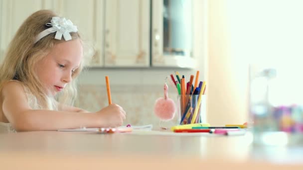 Schattig klein meisje zit aan de tafel en tekent met potloden. - Video