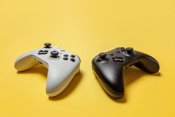 Λευκό και μαύρο δύο joystick σε κίτρινο φόντο. Αντίληψη για τον έλεγχο των βιντεοπαιχνιδιών - Φωτογραφία, εικόνα