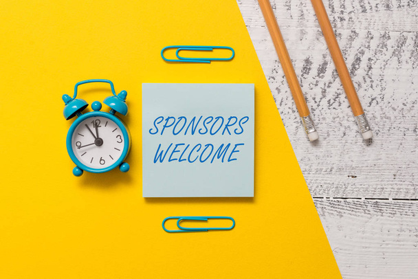 Text sign showing Sponsors Welcome. Conceptual photo announcing that you accept investing in your company Notepad clips colored paper sheet markers alarm clock wooden background. - Photo, Image