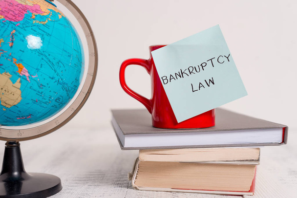 Writing note showing Bankruptcy Law. Business photo showcasing Designed to help creditor in getting the asset of the debtor Globe map world earth cup blank sticky note stacked books wooden table. - Photo, Image