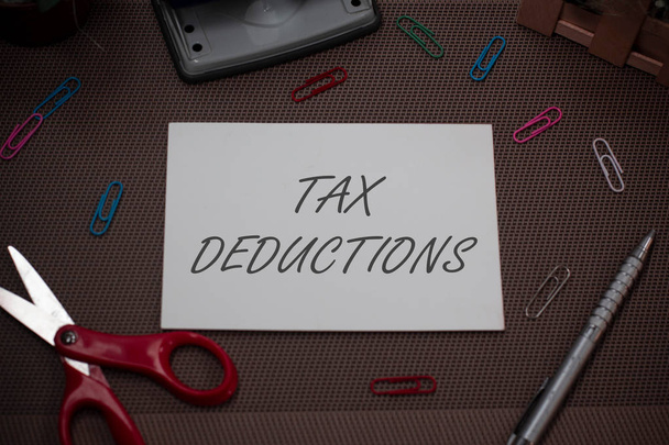 Handwriting text writing Tax Deductions. Concept meaning an amount or cost that subtracted from someone s is income Scissors and writing equipments plus plain sheet above textured backdrop. - Photo, Image
