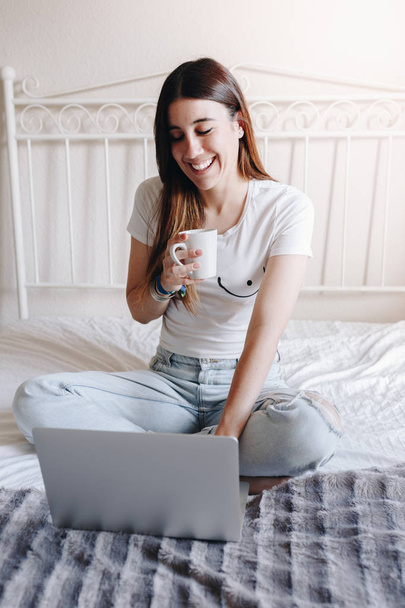 Счастливая веселая женщина смотрит смешной фильм на обычном ноутбуке, громко смеется и пьет кофе
 - Фото, изображение