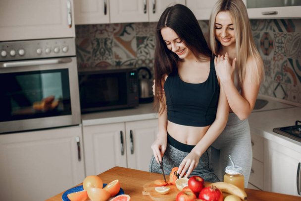 Sports girlss in a kitchen with fruits - Foto, afbeelding