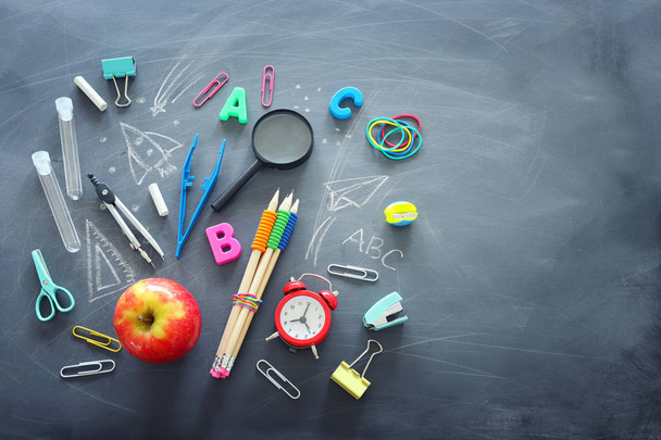 education and back to school concept. shapes cut from paper and painted of backpack, books, chemistry flask and apple over classroom blackboard with funny sketches. top view, flat lay - Photo, Image