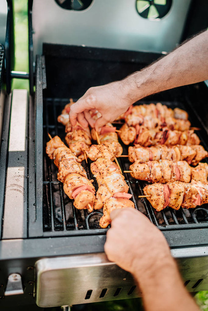 Close up details of man cooking chicken and meat on barbecue grill during summertime garden party - Foto, Bild