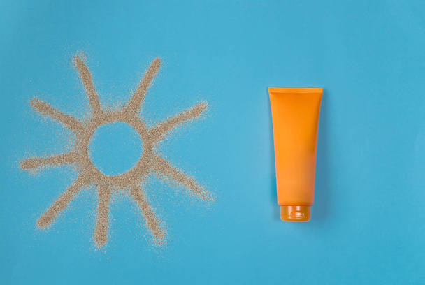 Sun drawn by the sand on blue background. Sunscreen on blue background. Top view. - Foto, immagini