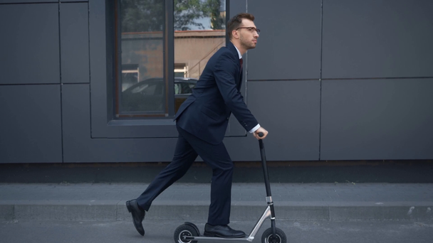 businessman in formal wear riding kick scooter near building - Filmagem, Vídeo