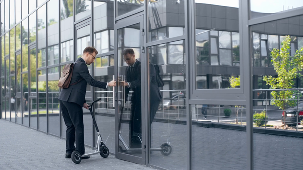 正式な着用のビジネスマンは、キックスクーターに乗って、ドアを開け、建物に入ります - 映像、動画