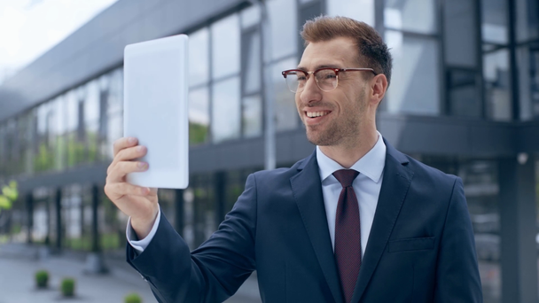 бизнесмен с цифровым планшетом с видеозвонком, показывая знак мира, разговаривая, улыбаясь и жестикулируя возле здания
 - Кадры, видео