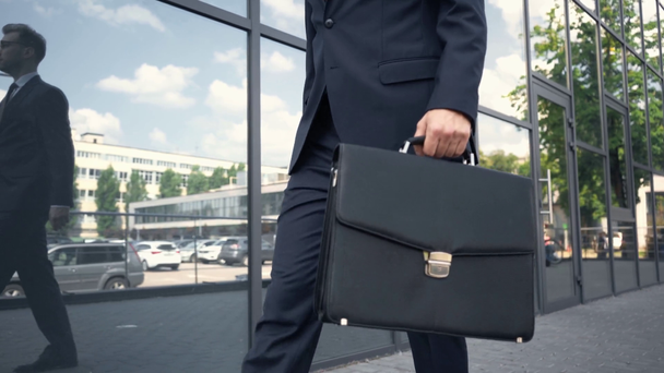 vista parcial del hombre de negocios en ropa formal caminando cerca del edificio con maletín
 - Metraje, vídeo