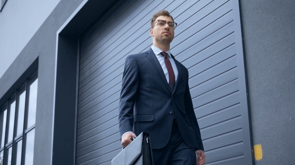 confident businessman in formal wear walking with briefcase near building - Metraje, vídeo