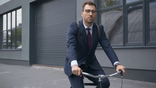 knappe zakenman met rugzak in formele slijtage paardrijden fiets in de buurt van gebouw - Video