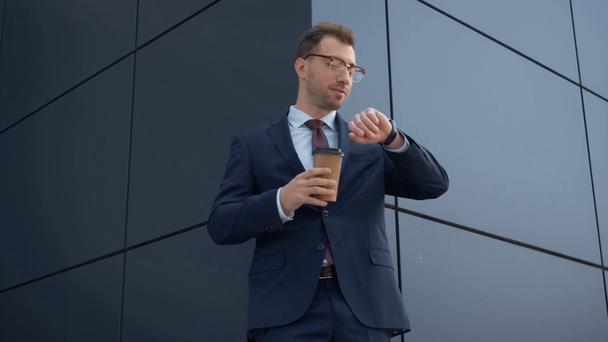 επιχειρηματίας να πίνει καφέ για να πάει και να κοιτάζει το ρολόι κοντά στο κτίριο - Πλάνα, βίντεο