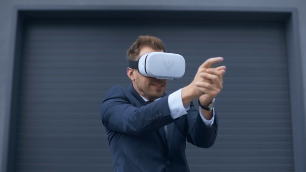 businessman in Virtual reality headset imitating shooting with gun near grey wall - Footage, Video