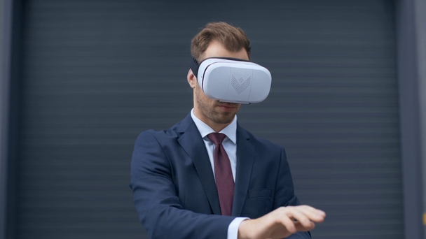 бізнесмен у гарнітурі віртуальної реальності жестикулює біля сірої стіни
 - Кадри, відео