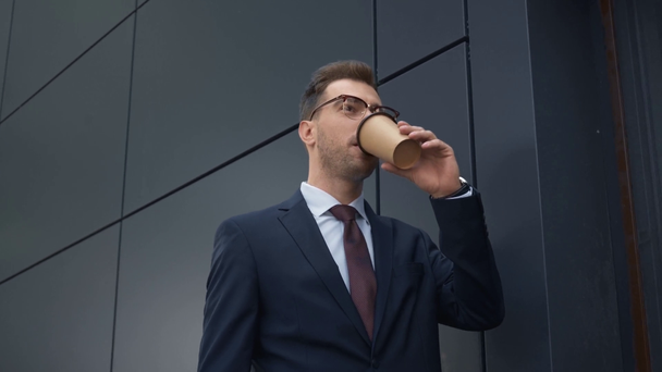 guapo hombre de negocios beber café para ir mientras camina cerca de la pared gris
 - Imágenes, Vídeo