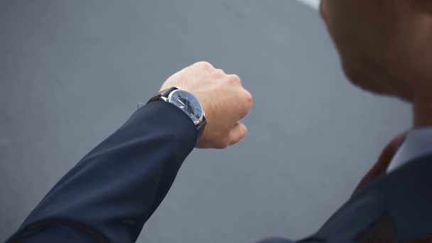Вид сзади бизнесмена, поднимающего руку и смотрящего на часы в сером
 - Кадры, видео